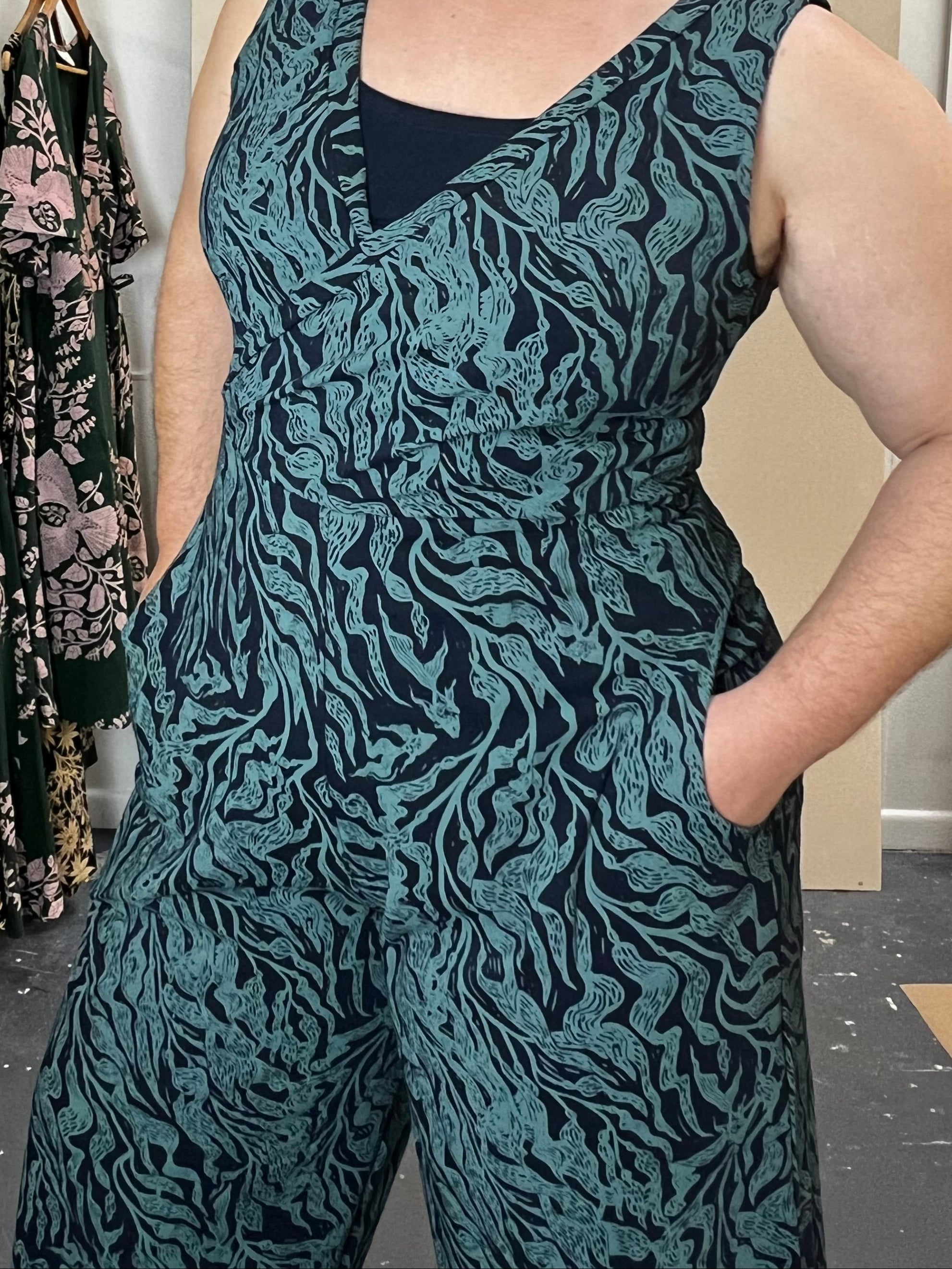 Woman wearing a patterned dress standing next to a rack of similar dresses.