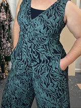 Woman wearing a patterned dress standing next to a rack of similar dresses.
